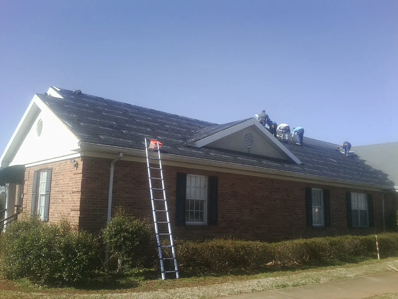 Crew tearing shingles off a brick ranch roof with a ladder set — Emergency Roof Repair work by our crew in Upton