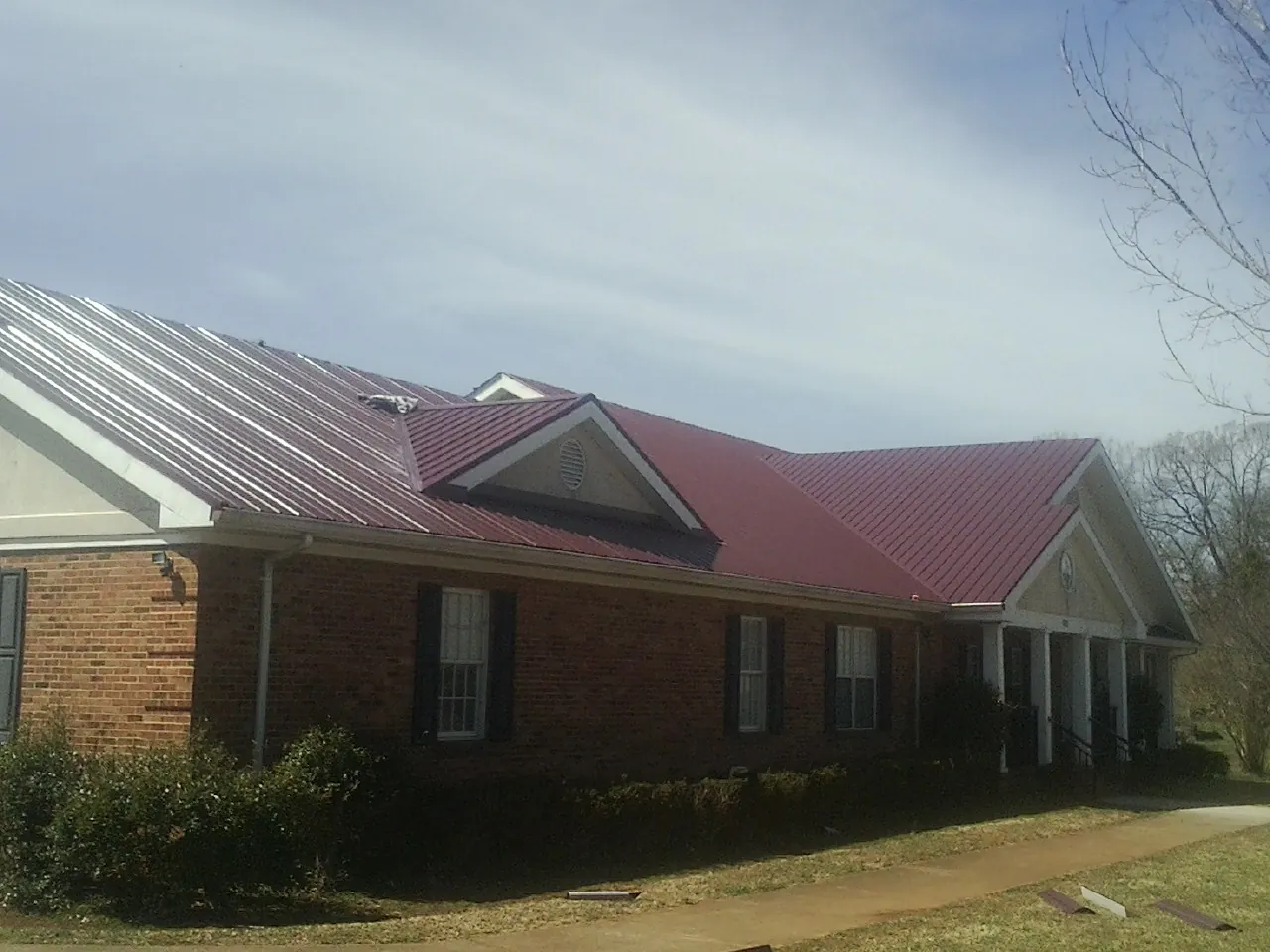 Red metal roof with gabled entries on a long brick building, from a Hail Damage Roof Repair job in Upton